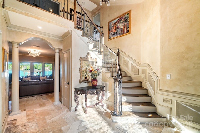 stairs featuring a towering ceiling, crown molding, decorative columns, arched walkways, and stone tile floors