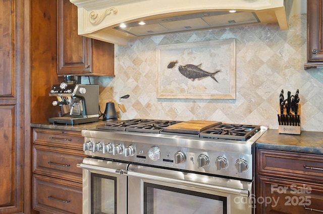 kitchen featuring premium range hood, double oven range, decorative backsplash, and dark countertops