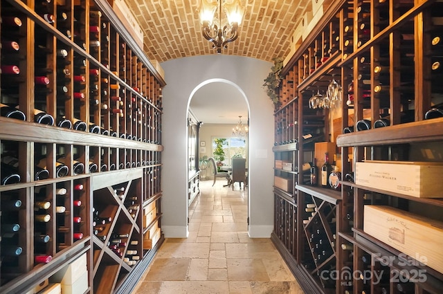 wine room with baseboards, a notable chandelier, brick ceiling, vaulted ceiling, and stone tile floors