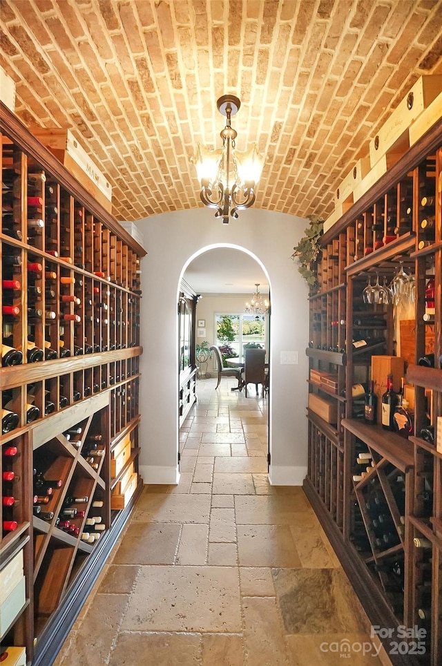 wine room featuring arched walkways, a notable chandelier, baseboards, and stone tile flooring