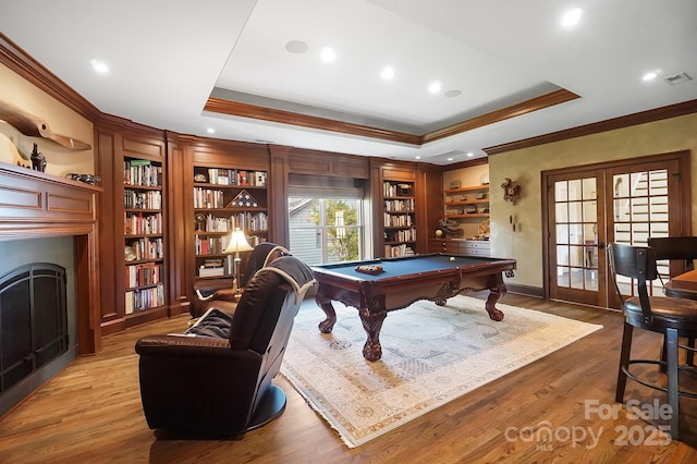 rec room featuring visible vents, ornamental molding, a fireplace, a tray ceiling, and french doors