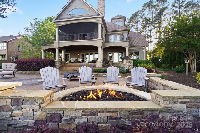 rear view of house featuring an outdoor fire pit, a patio, stone siding, a balcony, and a chimney