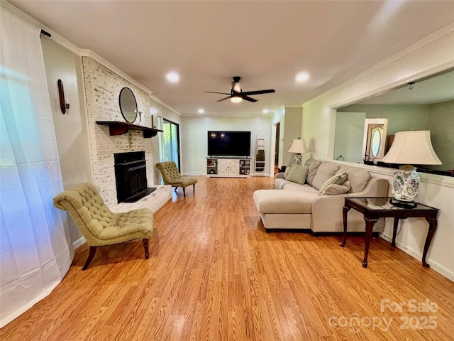 living room featuring a brick fireplace, light wood-style floors, crown molding, and ceiling fan