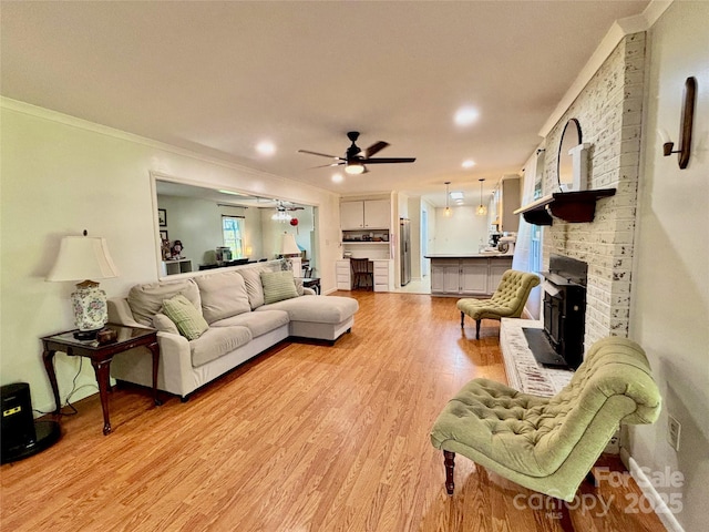 living room with light wood-style floors, crown molding, a ceiling fan, a brick fireplace, and baseboards