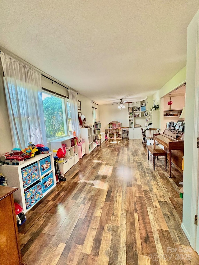 rec room with a textured ceiling, wood finished floors, and ceiling fan