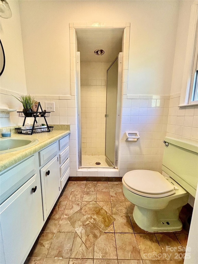 bathroom featuring a stall shower, wainscoting, tile walls, and toilet