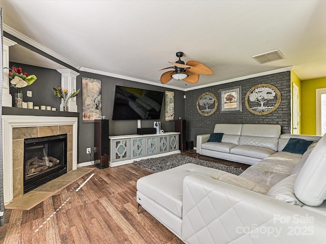 living area with visible vents, a ceiling fan, crown molding, wood finished floors, and a tile fireplace