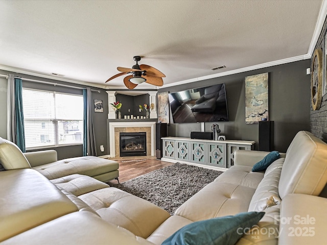 living area featuring visible vents, a ceiling fan, wood finished floors, and a tile fireplace
