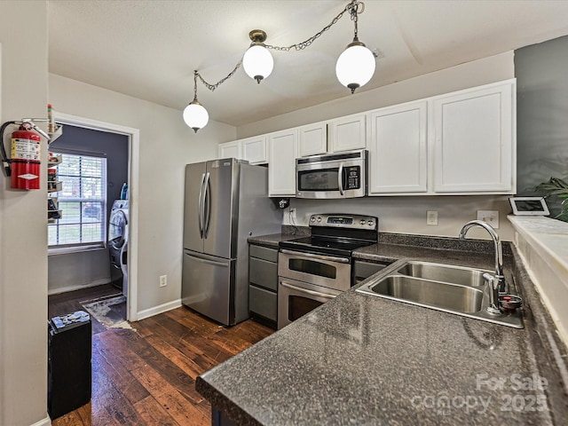 kitchen with dark wood-type flooring, white cabinetry, dark countertops, a sink, and stainless steel appliances