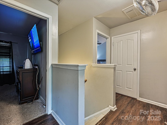 hallway with wood finished floors, visible vents, baseboards, and an upstairs landing