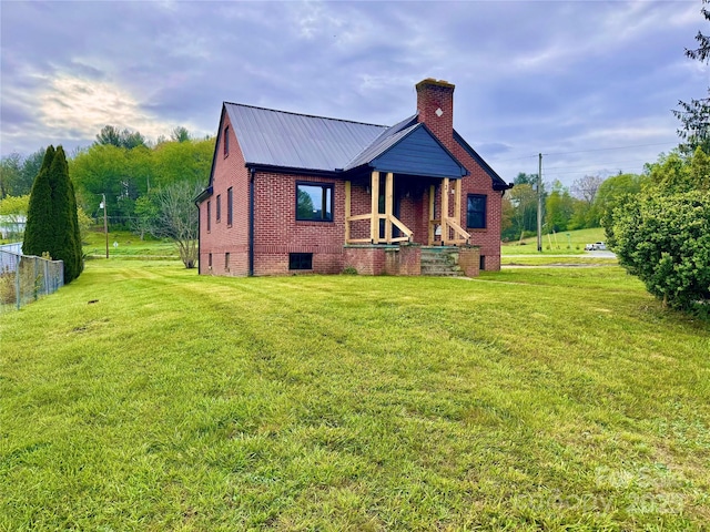 rear view of property featuring a chimney, brick siding, a yard, and metal roof