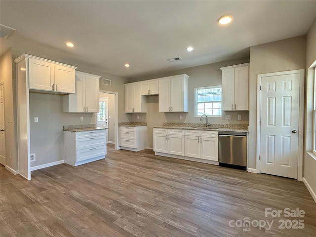 kitchen with wood finished floors, stainless steel dishwasher, a sink, and white cabinets