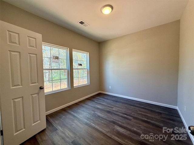 empty room with dark wood-style flooring, visible vents, and baseboards