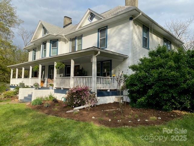 view of front of home featuring a chimney, covered porch, and a front yard