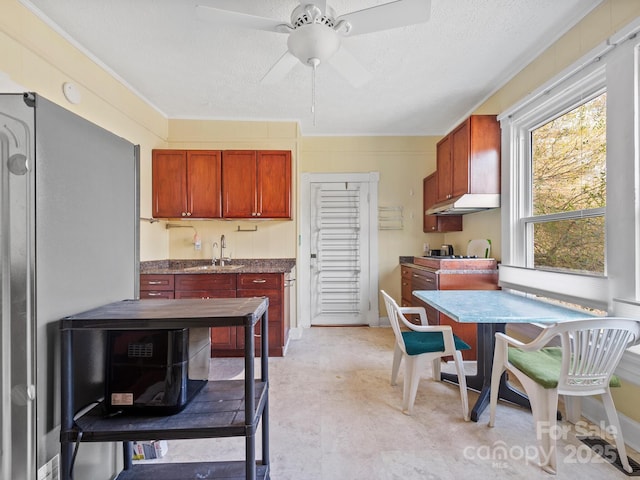 kitchen featuring freestanding refrigerator, a textured ceiling, a ceiling fan, under cabinet range hood, and a sink