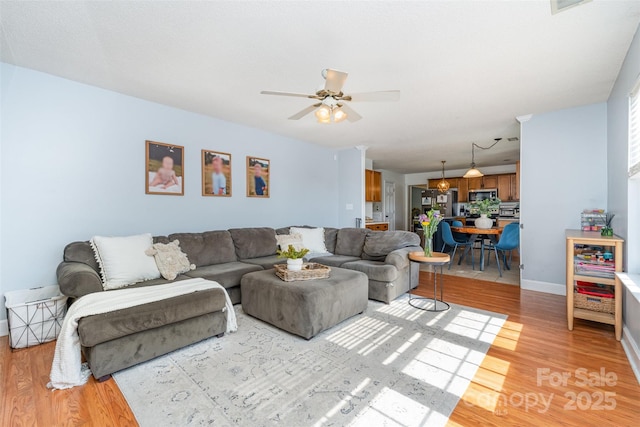 living area with baseboards, a ceiling fan, and light wood-style floors