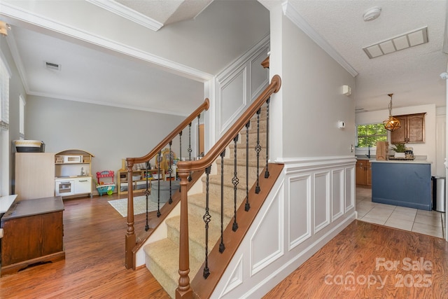 stairway featuring wood finished floors, visible vents, and crown molding