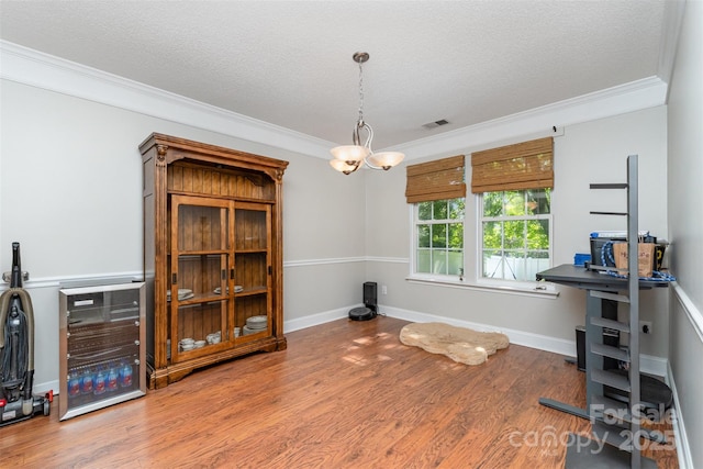 interior space featuring wood finished floors, a textured ceiling, crown molding, and visible vents