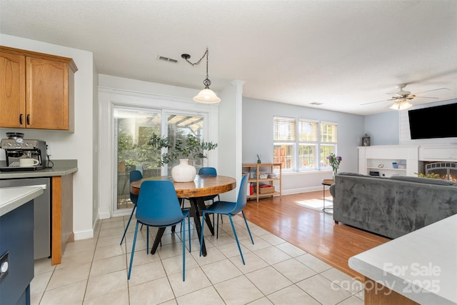dining area featuring baseboards, visible vents, a warm lit fireplace, ceiling fan, and light tile patterned floors