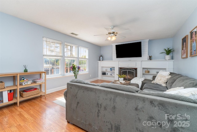 living area featuring a ceiling fan, light wood finished floors, a fireplace, baseboards, and visible vents