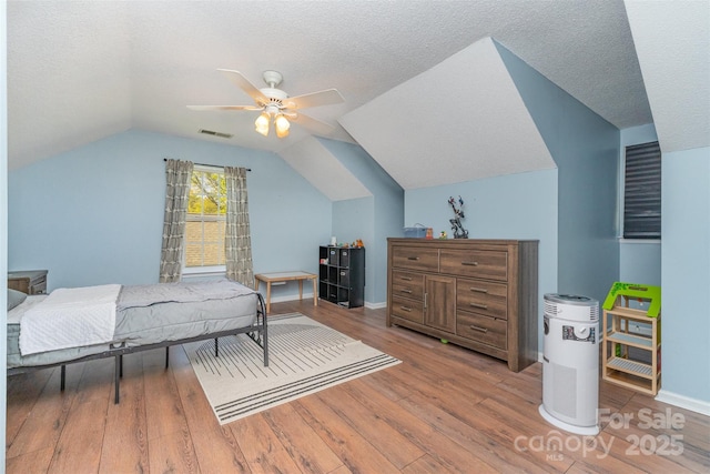 bedroom with vaulted ceiling, wood finished floors, visible vents, and a textured ceiling