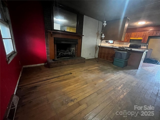kitchen featuring light countertops, a peninsula, a fireplace, brown cabinets, and hardwood / wood-style floors
