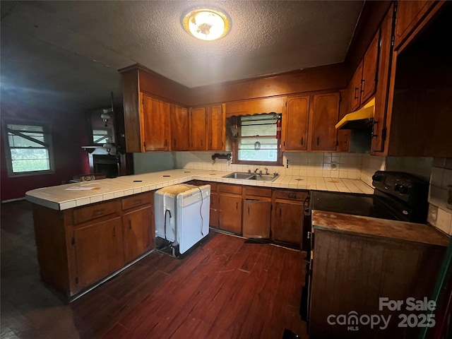 kitchen featuring a peninsula, under cabinet range hood, a sink, and brown cabinets