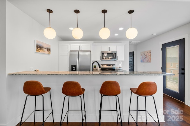 110 Hayden Way, Asheville, NC 28803 - kitchen with white cabinets, decorative light fixtures, appliances with stainless steel finishes, a kitchen bar, and dark wood-type flooring