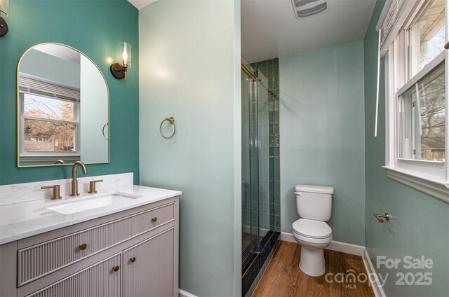full bath with vanity, toilet, tiled shower, visible vents, and wood finished floors
