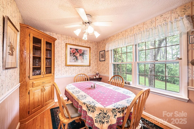 dining area with a textured ceiling, wallpapered walls, wainscoting, and wood finished floors