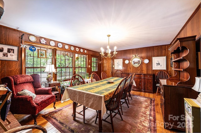 dining room featuring wooden walls, hardwood / wood-style flooring, and a chandelier