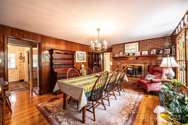 dining space with brick wall, a brick fireplace, wooden walls, an inviting chandelier, and hardwood / wood-style floors