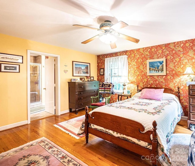 bedroom with a ceiling fan, wood finished floors, baseboards, ensuite bathroom, and wallpapered walls