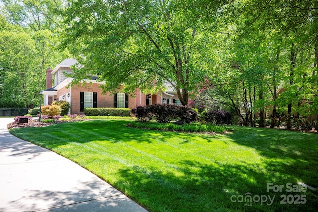 view of front of house with a chimney, brick siding, fence, and a front lawn
