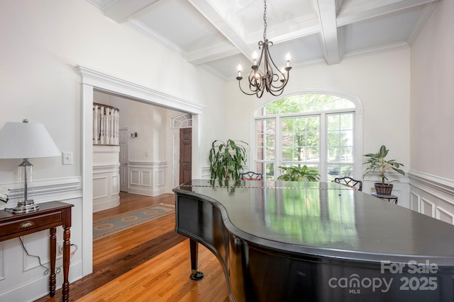 dining area with beam ceiling, light wood-style floors, a notable chandelier, coffered ceiling, and a wainscoted wall