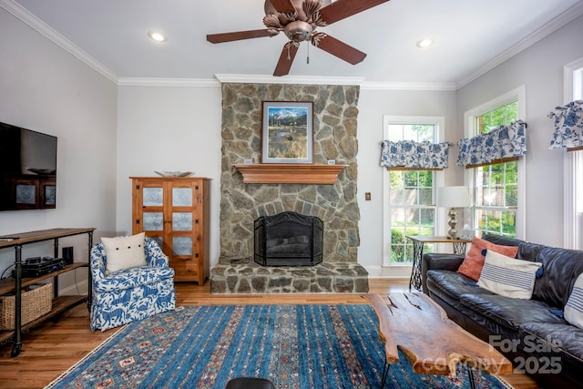 living area with crown molding, ceiling fan, a stone fireplace, and wood finished floors