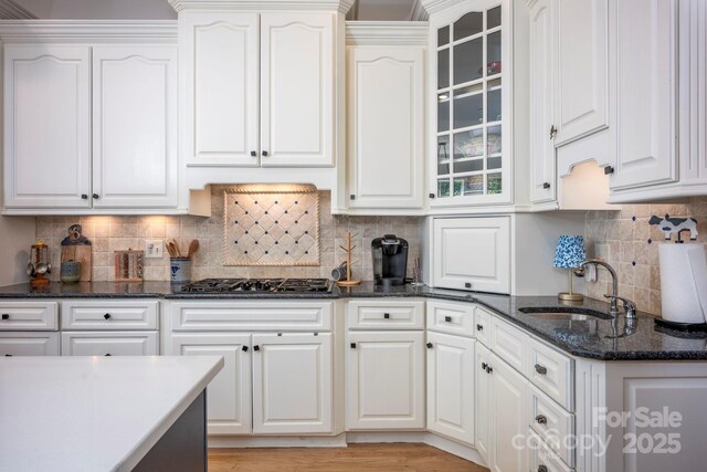 kitchen with glass insert cabinets, a sink, gas stovetop, and white cabinets