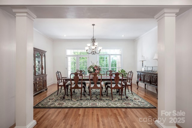 dining room featuring ornamental molding, a notable chandelier, decorative columns, and wood finished floors
