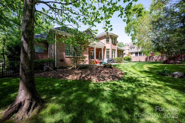 back of house featuring a lawn, fence, and brick siding
