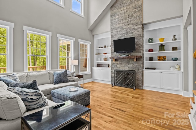 living area featuring a fireplace, built in shelves, baseboards, light wood-type flooring, and a towering ceiling
