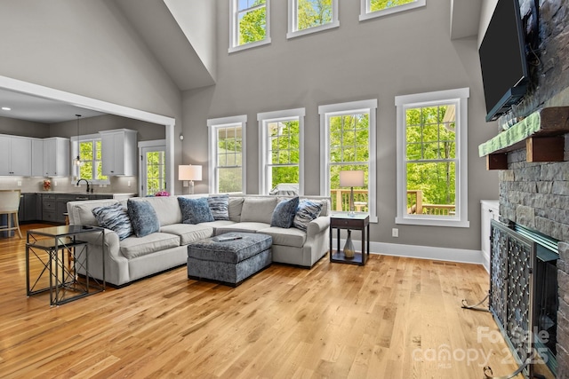 living room featuring visible vents, a healthy amount of sunlight, a stone fireplace, a high ceiling, and light wood-style flooring
