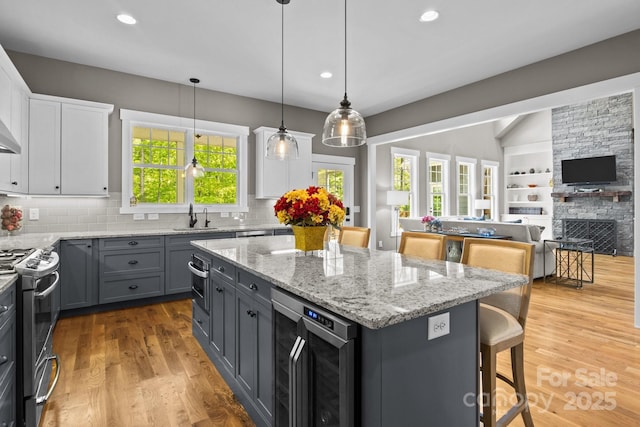 kitchen featuring wine cooler, stainless steel gas stove, white cabinets, a sink, and gray cabinetry