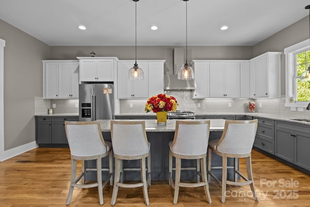 kitchen featuring decorative backsplash, a center island, wall chimney exhaust hood, gray cabinets, and appliances with stainless steel finishes