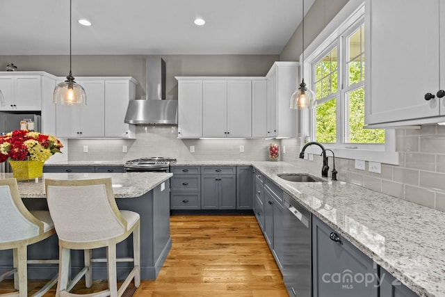kitchen featuring a breakfast bar, a sink, gray cabinets, wall chimney exhaust hood, and stainless steel appliances