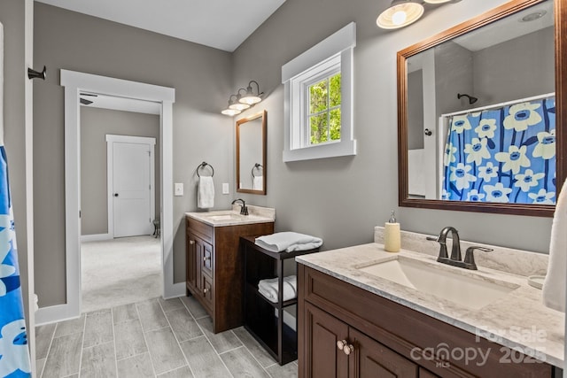 full bath with baseboards, a sink, two vanities, and curtained shower