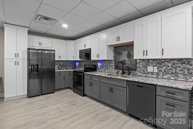kitchen with light stone counters, a sink, gray cabinets, and black appliances