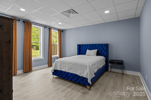 bedroom featuring baseboards, a drop ceiling, wood finished floors, and visible vents