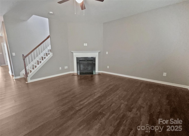 unfurnished living room with baseboards, ceiling fan, a fireplace, stairway, and wood finished floors