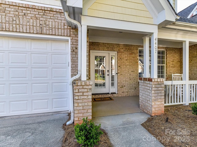 doorway to property with covered porch, brick siding, and a garage
