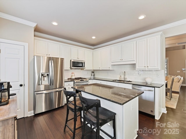 kitchen with white cabinetry, a sink, appliances with stainless steel finishes, dark wood-style floors, and ornamental molding